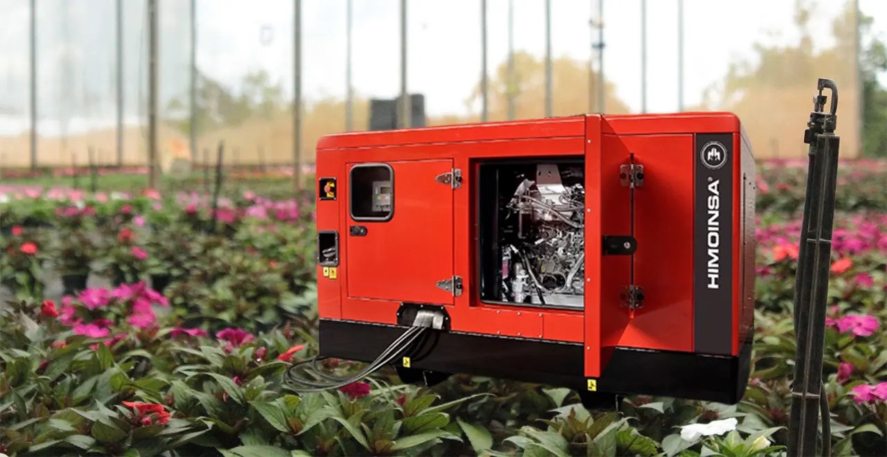 Gerador Himoinsa vermelho em operação dentro de uma estufa agrícola cercado por plantas floridas