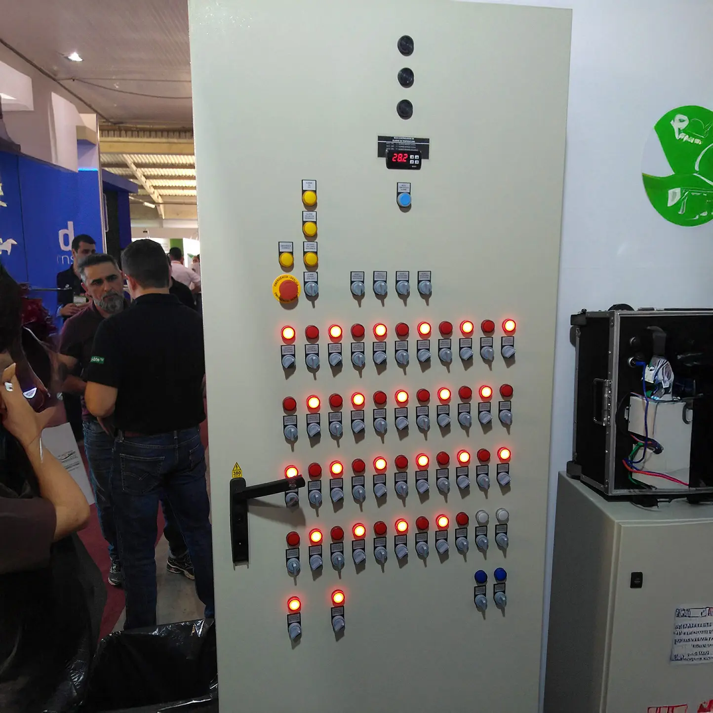 Painel de controle elétrico com indicadores LED acesos em um evento técnico, destacando sistemas de automação industrial